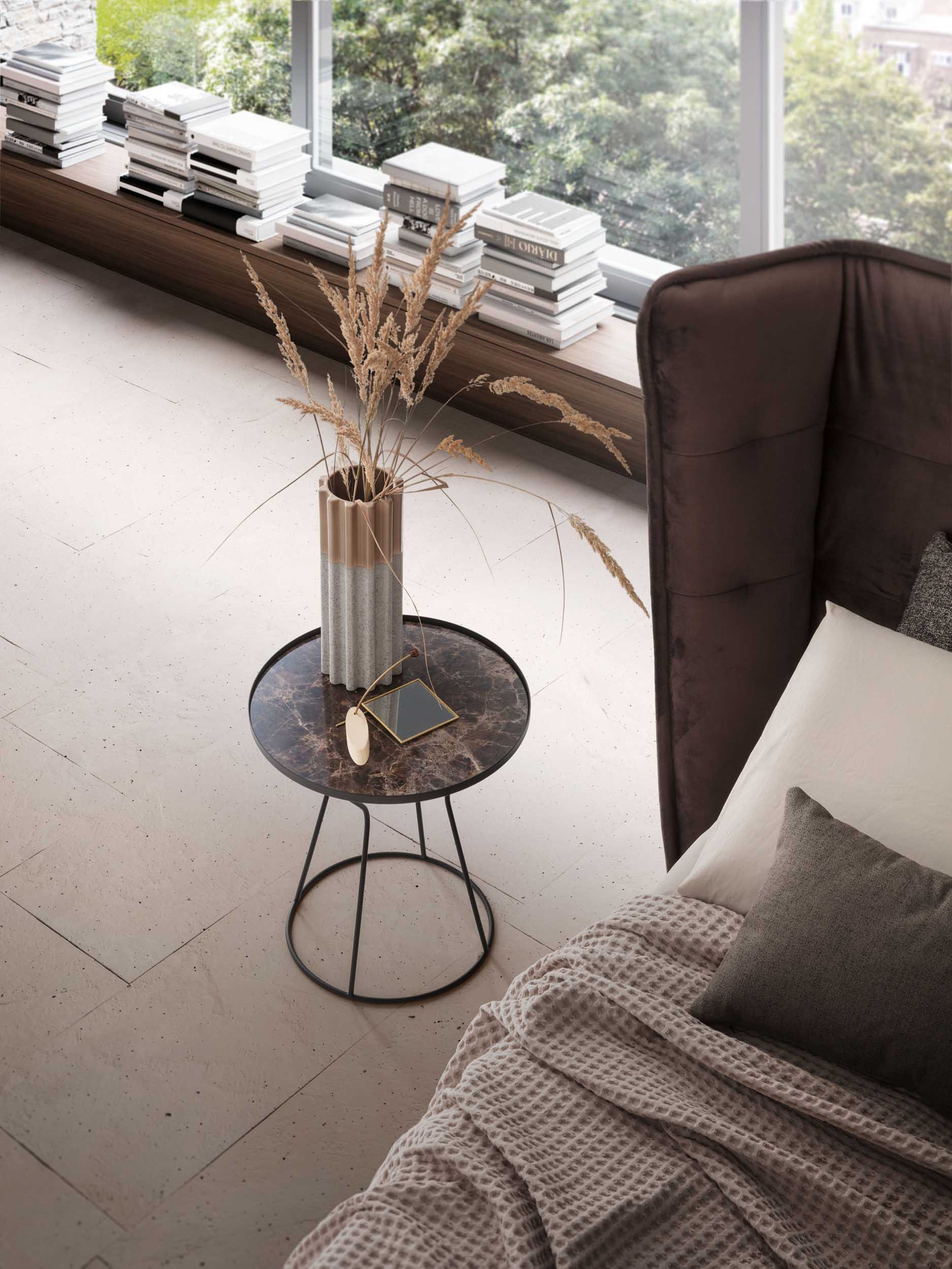 Round coffee table with an Emperador gres top and a slim metal structure. Placed in a bedroom.