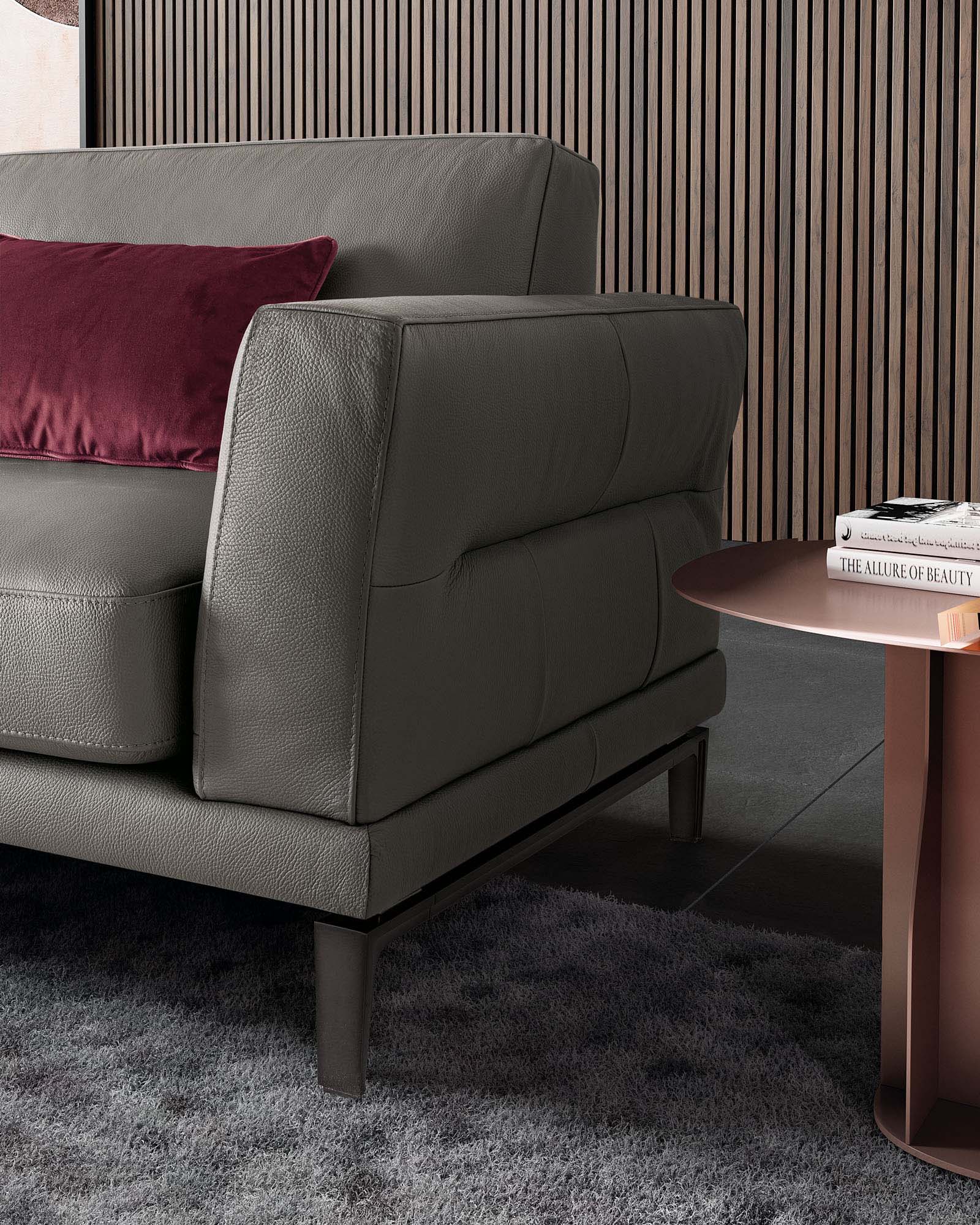Detail of the armrest of a grey leather sofa with high legs.