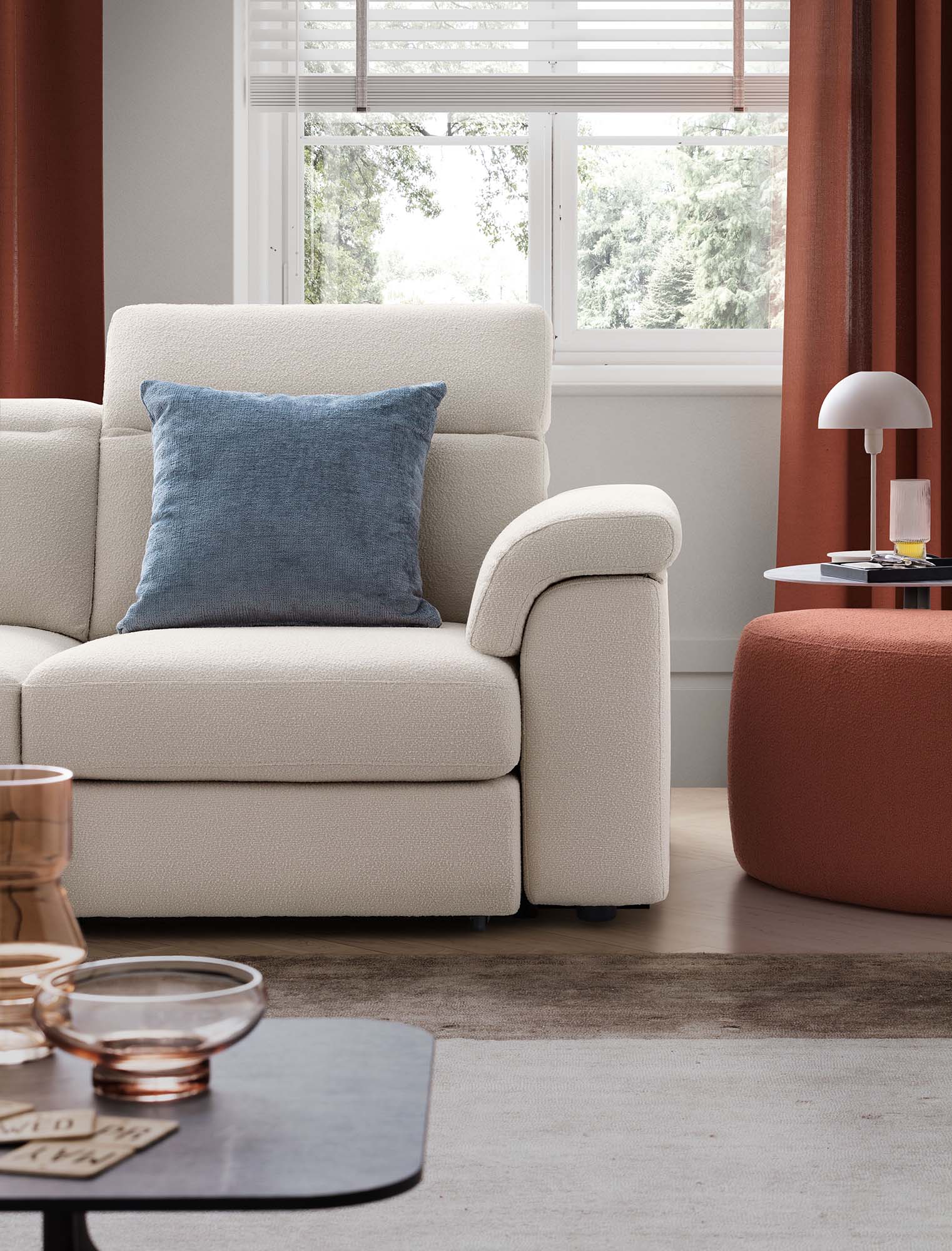 Detail of the seat of a white sofa in a modern, warm and welcoming living room composed of coffee tables, table lamps and brick-colored poufs