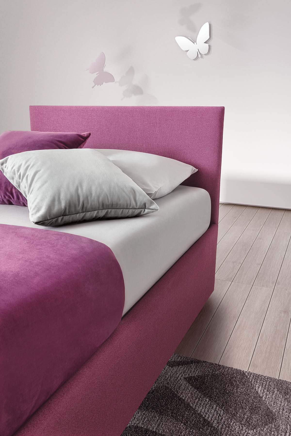 Detail of the super thin headboard of a pink single bed and silver cushions
