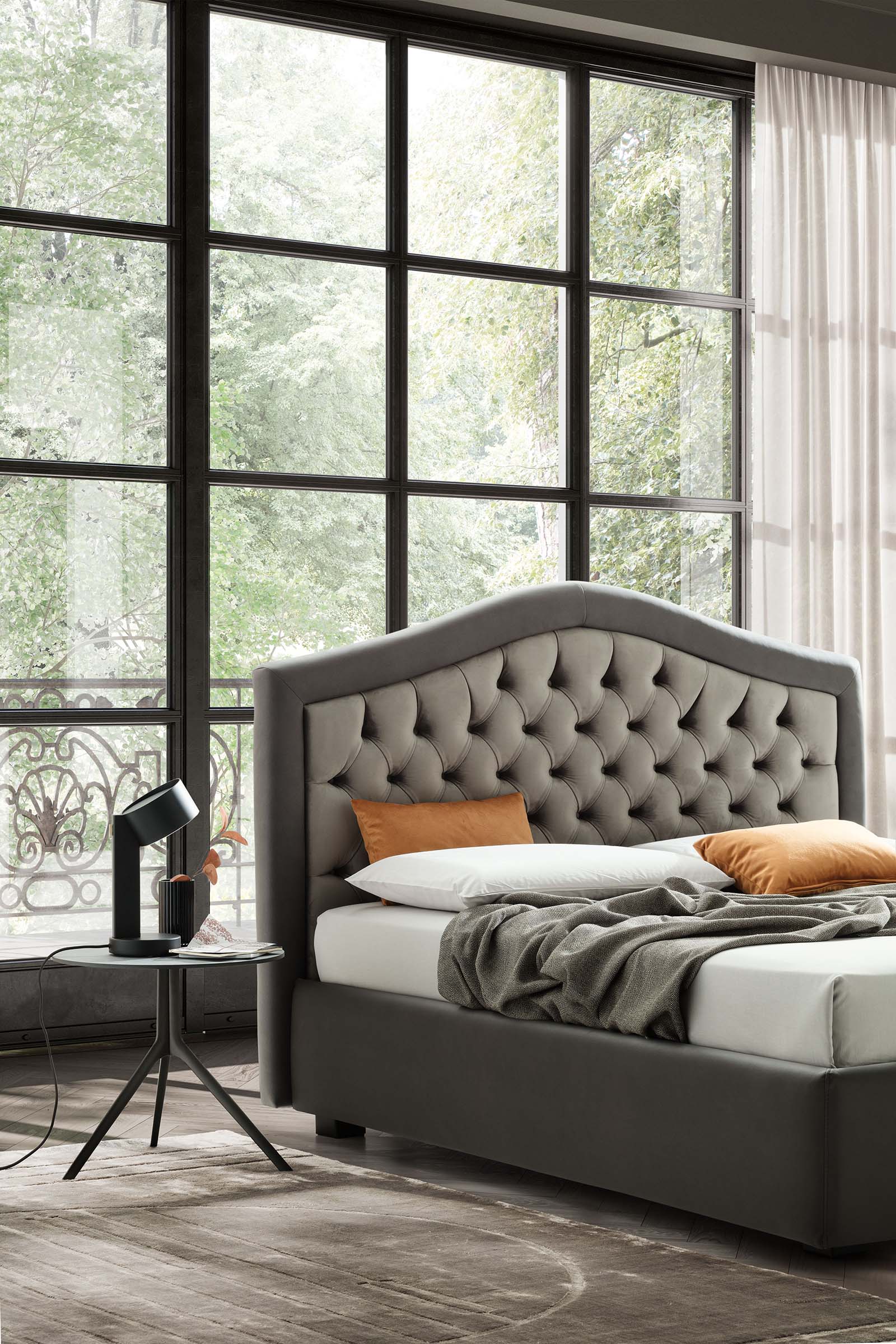 Room with large windows furnished with a gray Chesterfield-style bed and matching small table