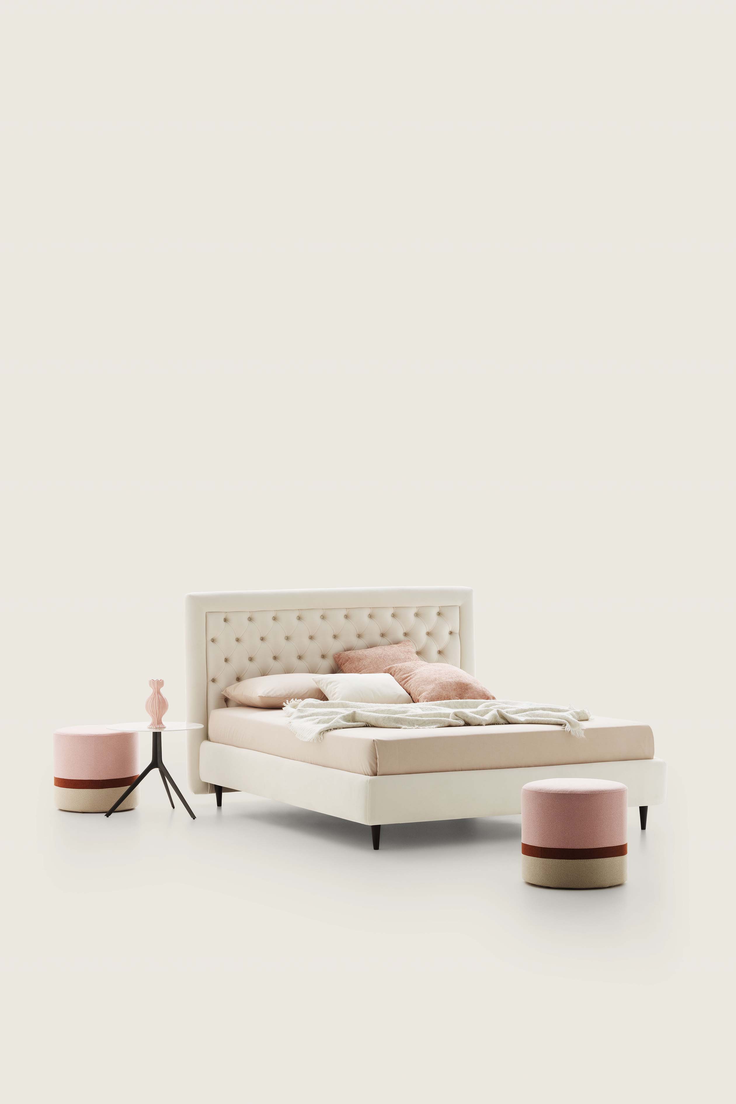 Double bed with capitonné upholstered in cream-colored fabric and matching poufs
