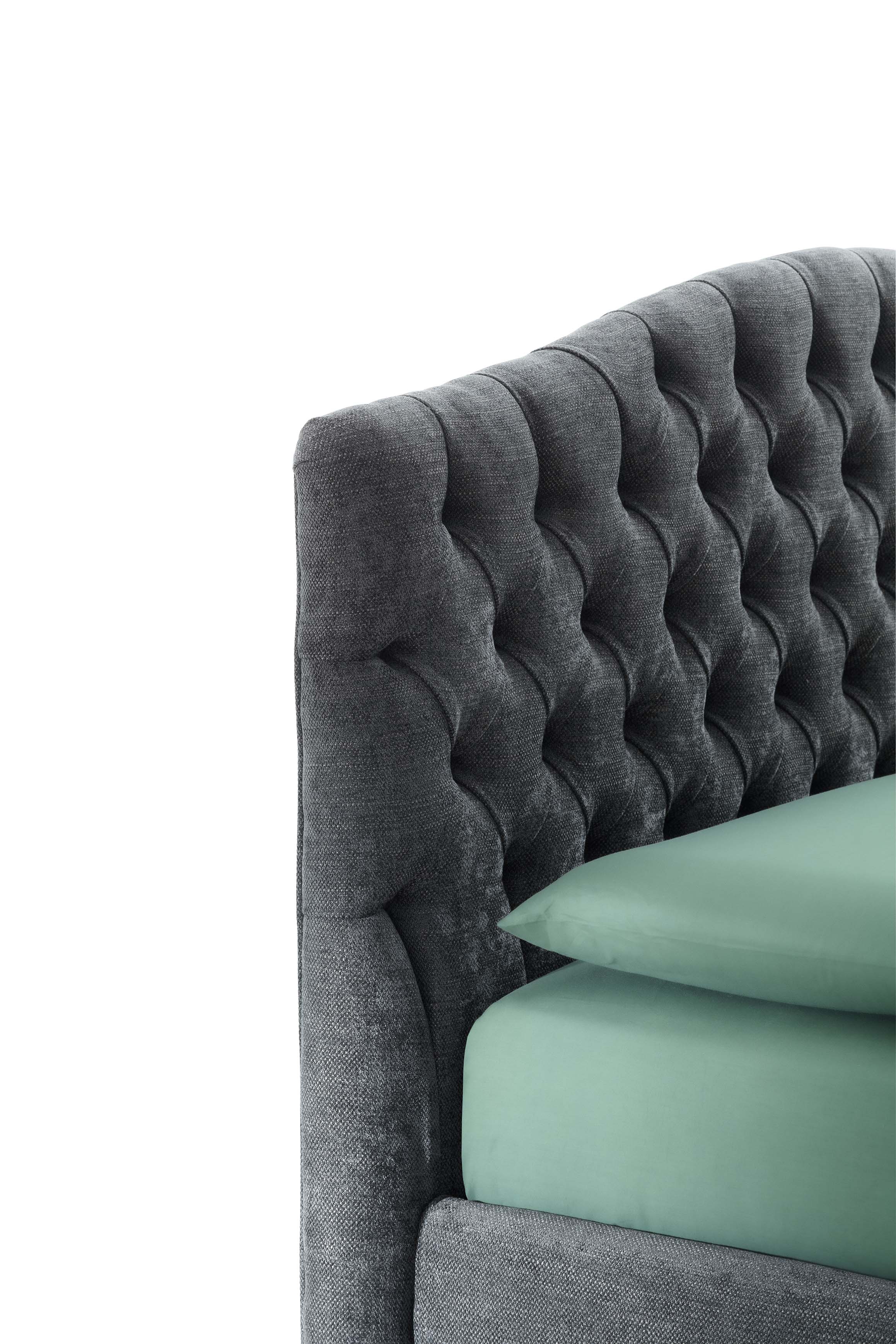Chesterfield detail of the high headboard of a gray fabric bed